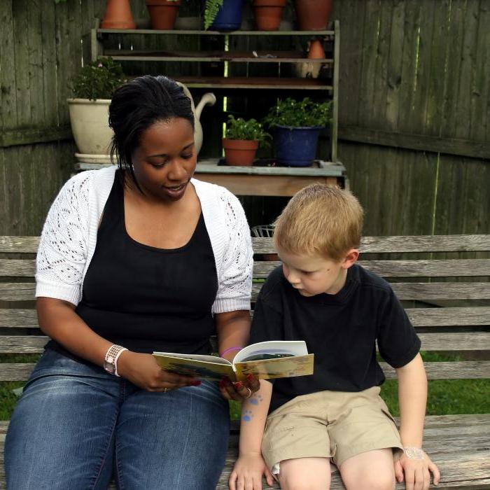 an african american woman and a young child sitting on a bench reading