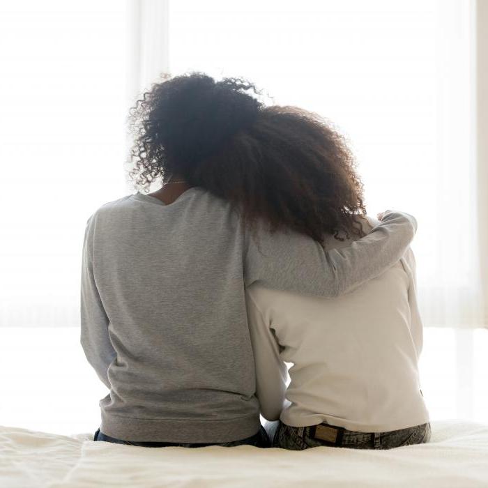 Back view of loving African American mother hug teen daughter sitting on bed